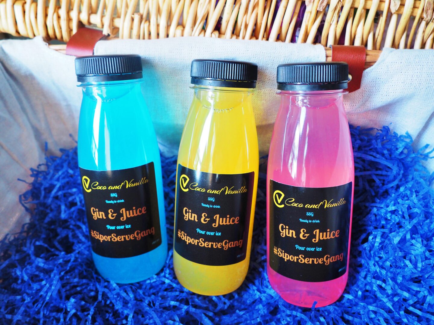 Three bottles containing cocktails, the colours are blue, yellow and pink 