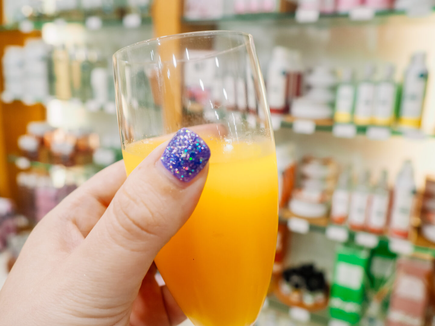 My hand with glitter purple nails holding a glass of orange